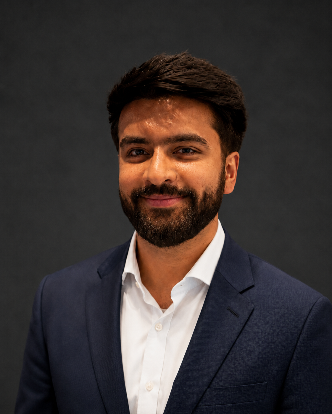 A headshot of Ansh Ankul against a black background in a navy suit.
